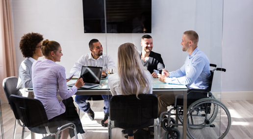 l'immagine raffigura una riunione di lavoro attorno ad un tavolo con diverse persone tra cui un soggetto in carrozzina